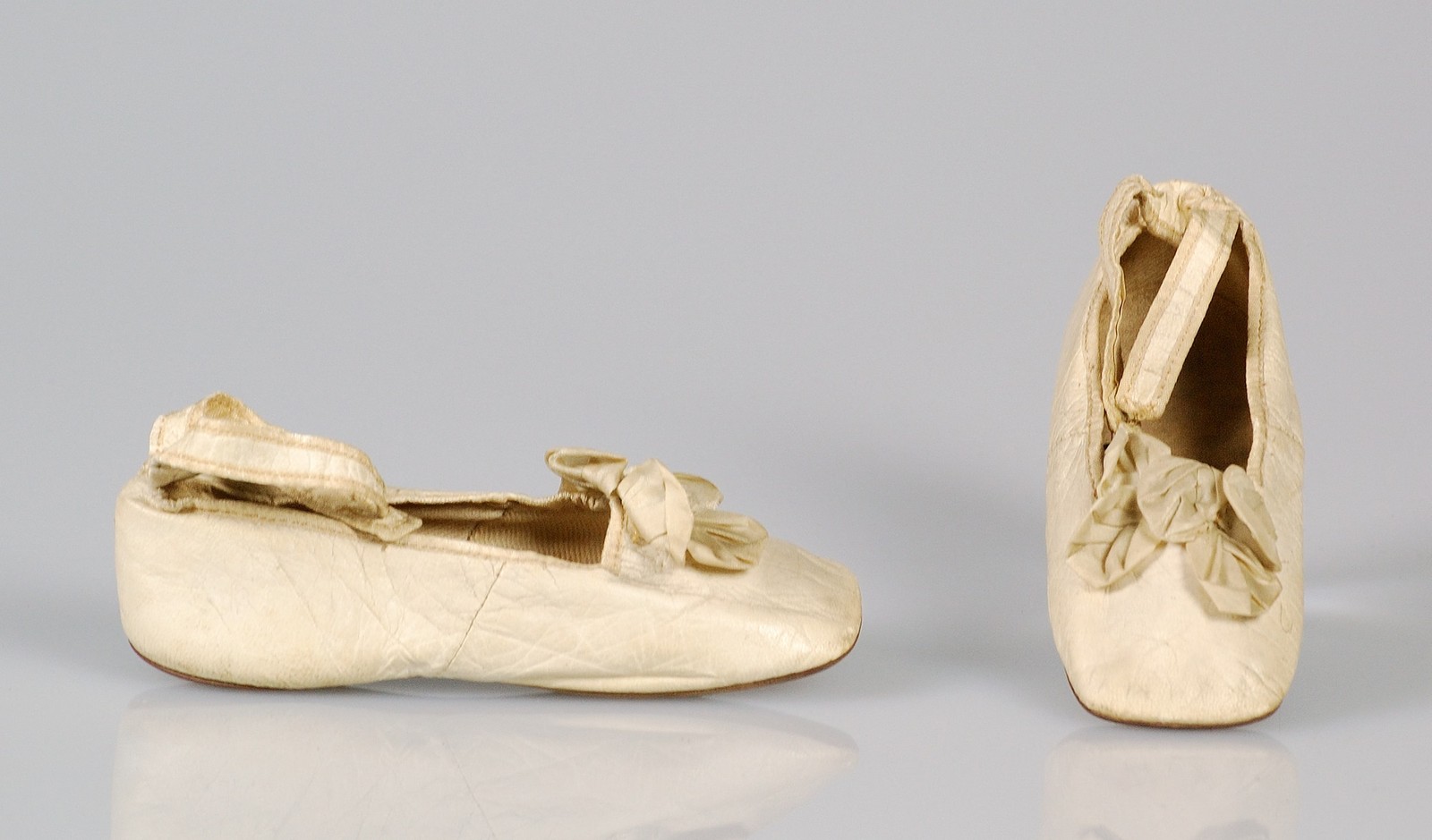 Pale shoes with bows and ankle straps, photographed as a museum object.
