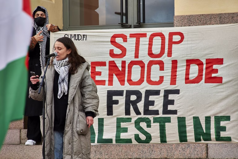 A speaker at a Helsinki Palestine solidarity demonstration beside a banner reading Stop Genocide, Free Palestine, October 21, 2023.