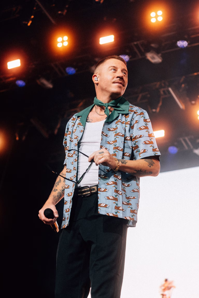 Macklemore holding a microphone beneath warm stage lights at Lollapalooza Berlin in 2023
