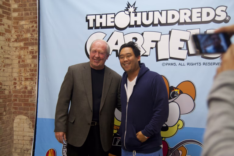 David Choe, right, and Jim Davis smiling together in front of a Garfield backdrop in 2010