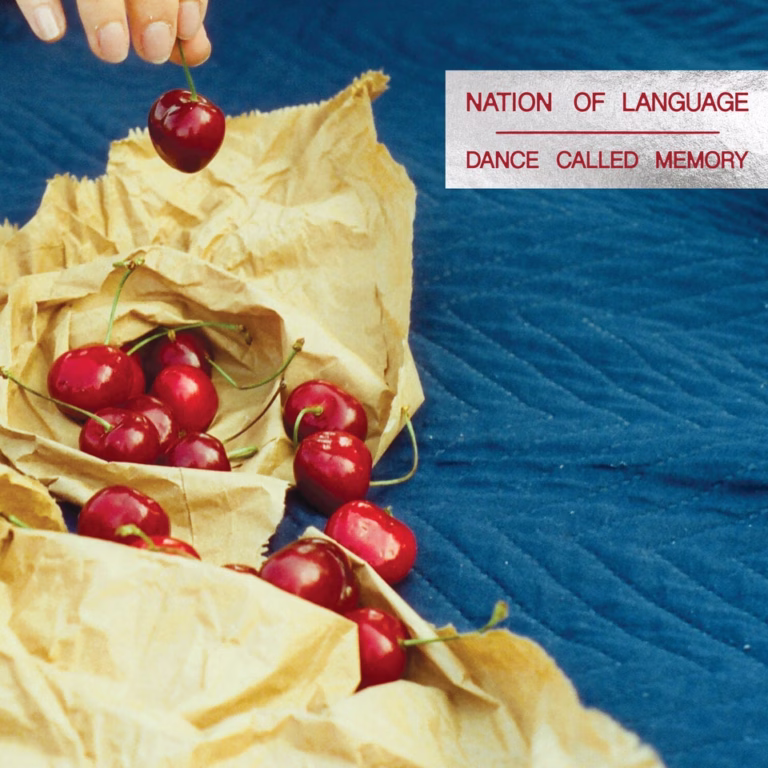 Red cherries on yellow paper against blue fabric on Nation of Language’s Dance Called Memory cover.