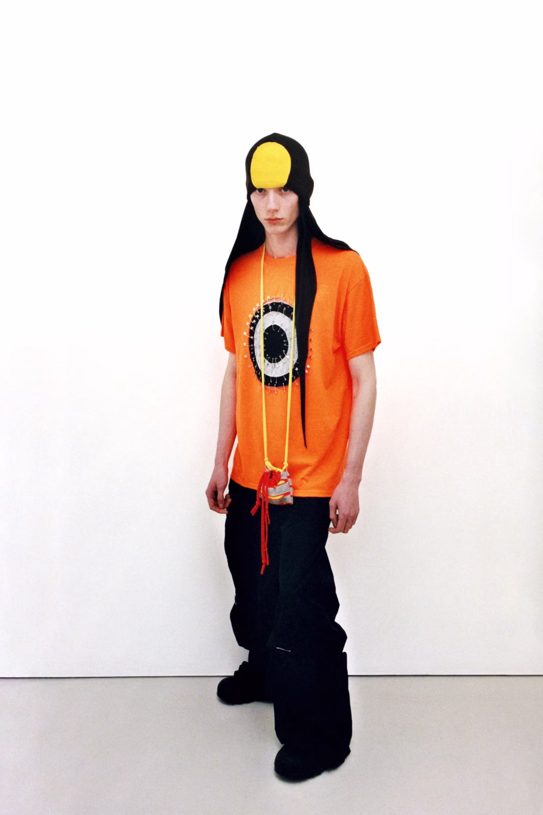 Model wearing a bright orange Jawara Alleyne top with black trousers and sculptural headwear
