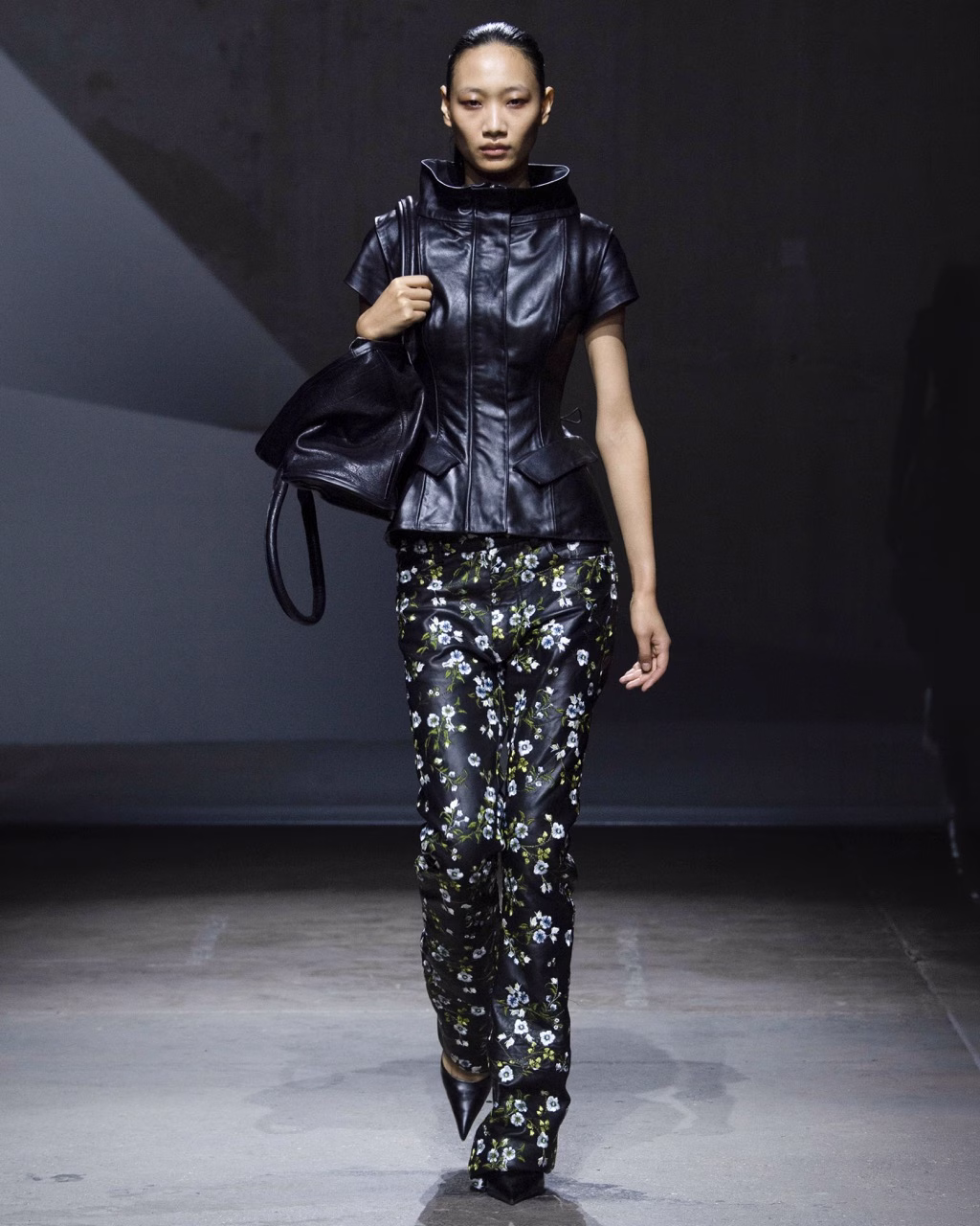 Model wearing a structured black jacket, floral trousers and a large black bag in Petra Fagerström’s Spring/Summer 2027 collection.