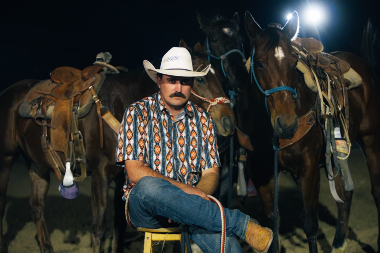 Wade Forster seated in a cowboy hat in front of saddled horses