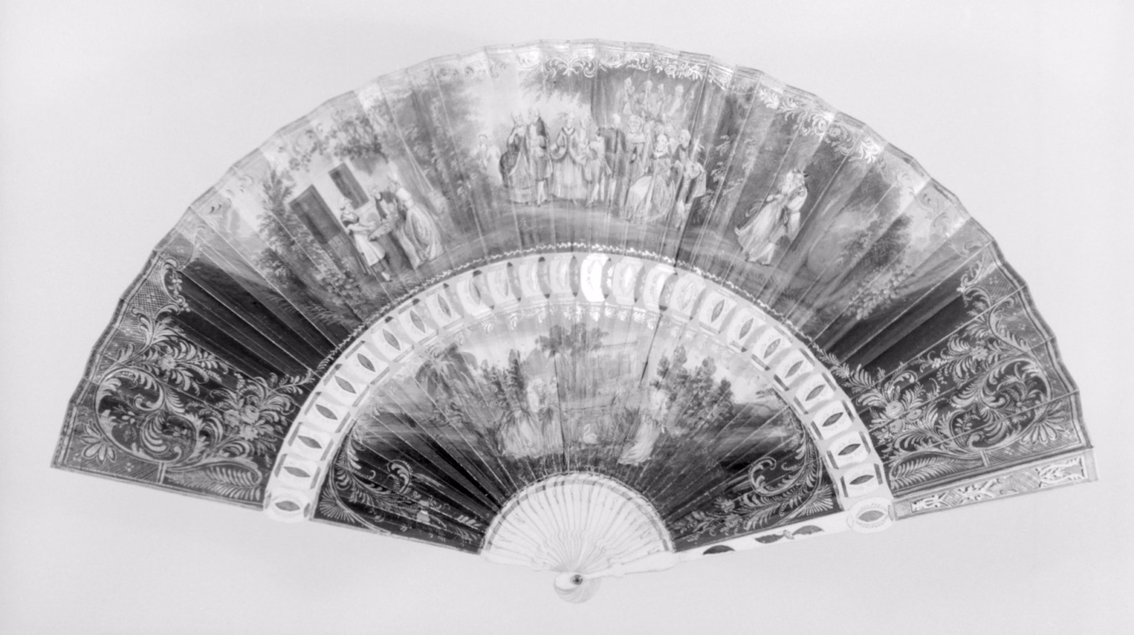 Black-and-white museum photograph of an open French folding fan, with a painted scene across the leaf and ornate radiating sticks.