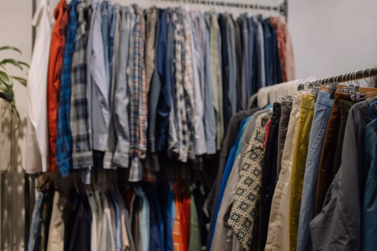 Secondhand shirts and trousers on clothing racks, showing varied colors, patterns and fabrics; no people are pictured.